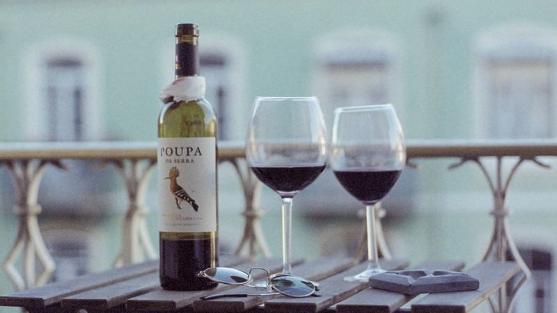 A bottle of Portuguese red wine and two glasses on a balcony table above a Lisbon street
