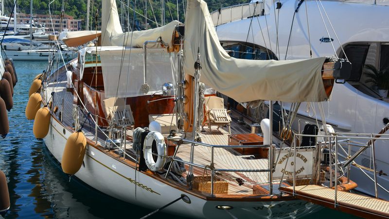 The varnished deck, sails and brass of a classic ketch moored beside a modern yacht