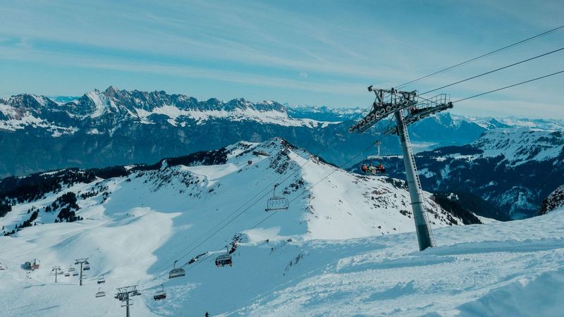 A chairlift climbing over the snowfields, a long jagged range of peaks beyond under a pale blue sky