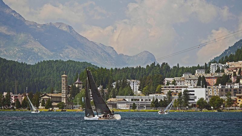 Racing yachts sailing on Lake St. Moritz in front of the town, its church tower and the forested mountains