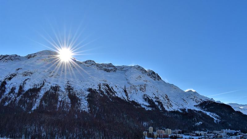 The winter sun bursting over a snowy mountain above the town of St. Moritz