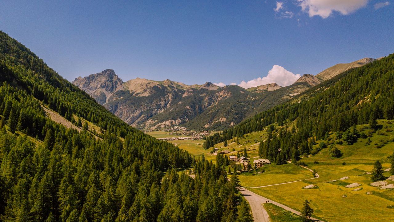 A green larch valley in the French Alps in summer, with chalets in the meadows and a village below the peaks
