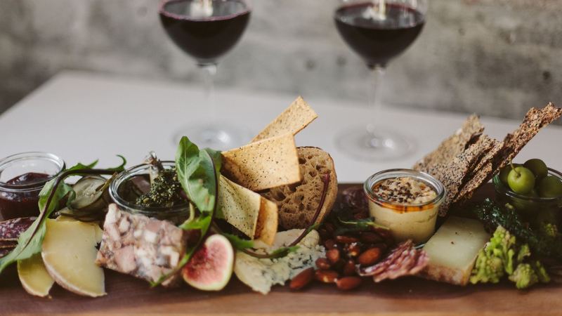 A board of cheeses, terrine, figs, olives and crisp breads, two glasses of red wine behind