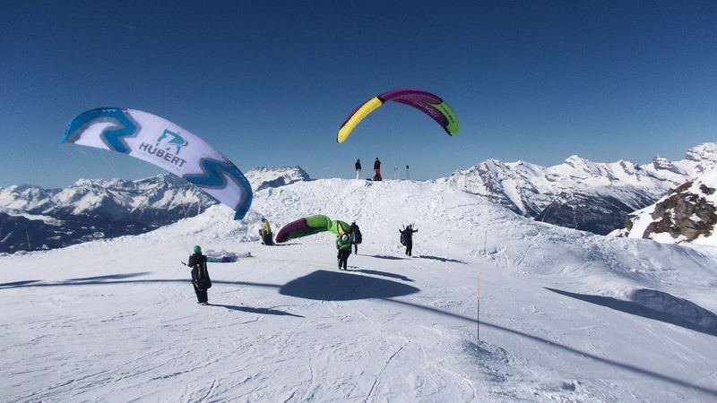 Paragliders laying out their wings on a snowy summit above the peaks of the Valais