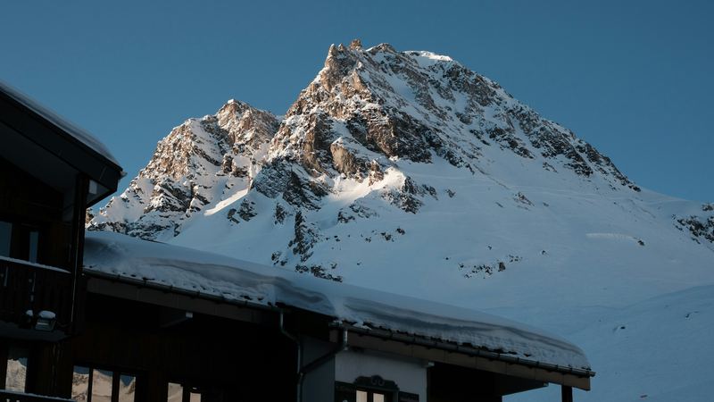 A snowy peak glowing in the morning sun above a chalet roof heavy with snow
