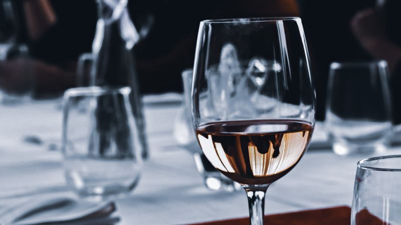 A glass of rosé on a white tablecloth among glasses and napkins in a restaurant