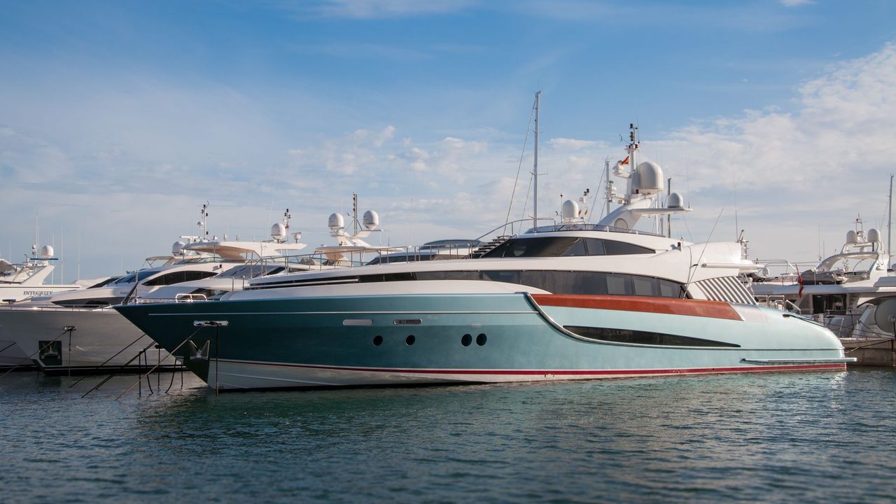 A sleek motor yacht in pale blue moored among superyachts in a Mediterranean marina