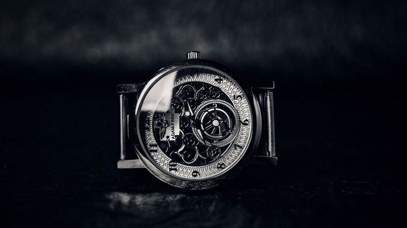 A skeleton watch with an engraved dial and visible movement on a dark background