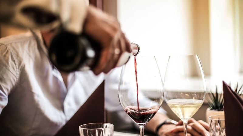 Red wine poured into a large glass beside a glass of white at a restaurant table by the window